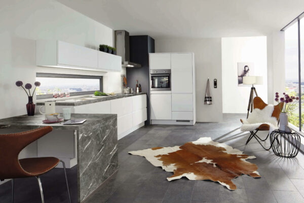 Weiß-matte Küche mit schmalen Hängeschränken, grauer Arbeitsplatte und Essbereich.